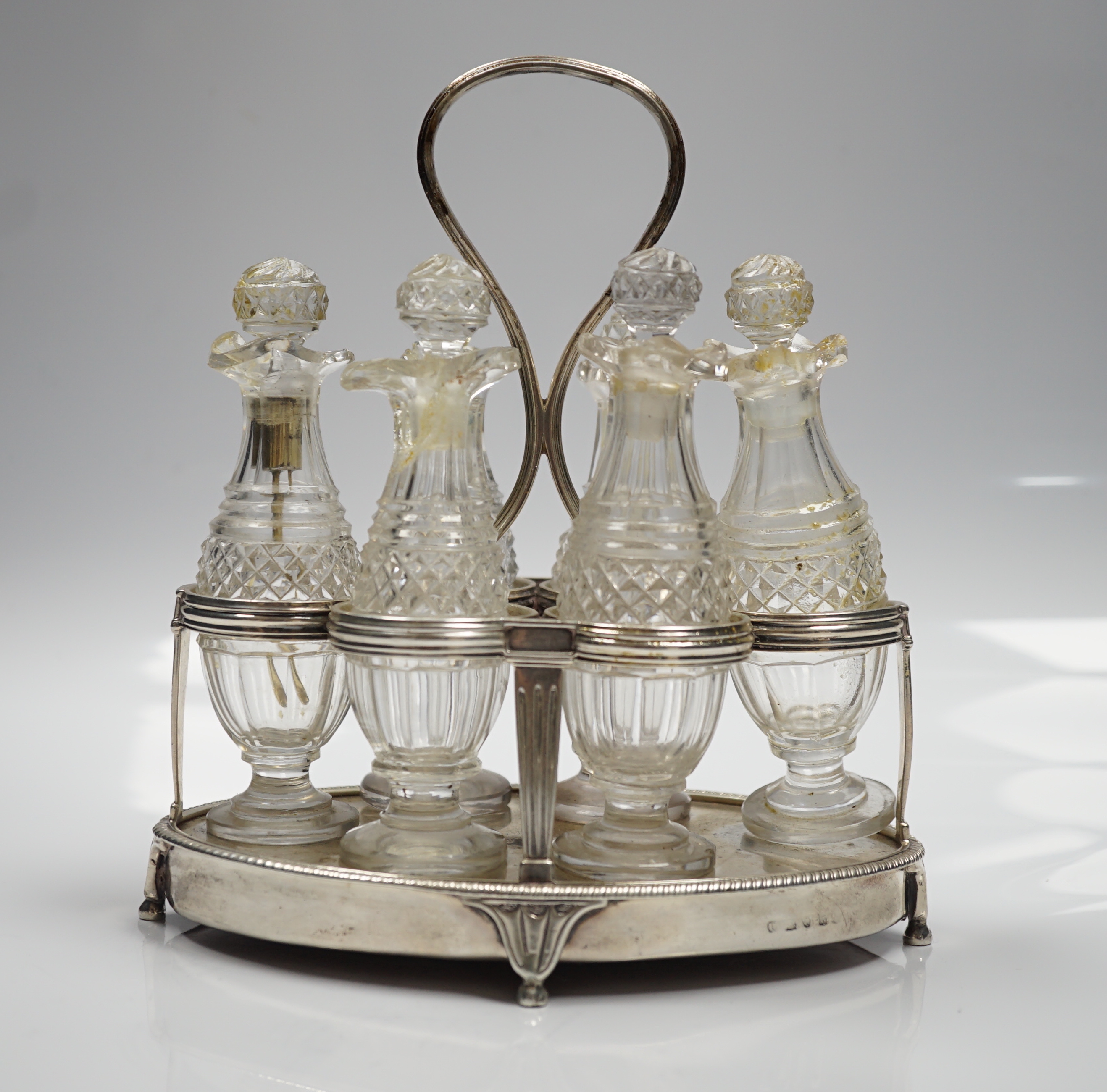 A George III silver mounted oval cruet stand, maker P?, London, 1802, with reeded ring handle and gadrooned border, with six cut glass bottles and stoppers (some damage), height 20cm.